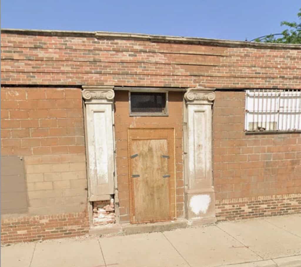 Historic brick building with boarded-up door and decorative columns.